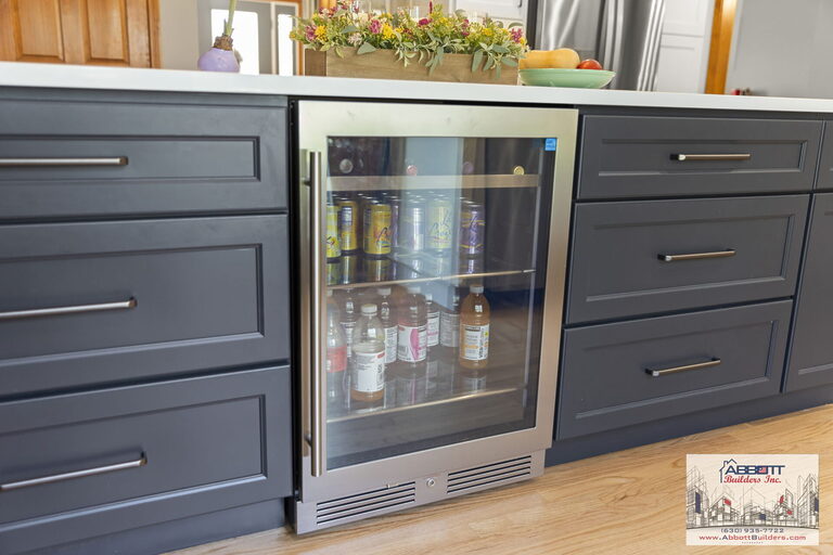 Built-in stainless steel beverage fridge installed in a navy kitchen island with shaker drawers and quartz countertop, part of a luxury kitchen renovation by Abbott Builders in Villa Park, IL.